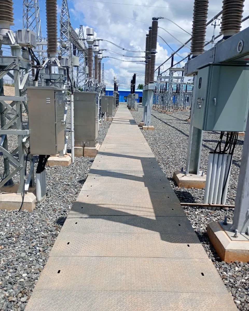 A walkway between rows of high voltage insulators, disconnect switches and control cabinets inside an electrical substation.
